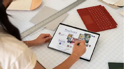 Eine Person arbeitet mit einem Stift auf einem Tablet mit Moodboard- und Branding-Elementen, umgeben von Lineal und roter Tastatur.