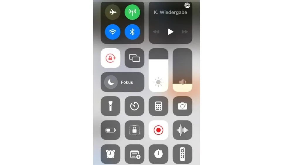 Ein Smartphone-Bildschirm zeigt das Kontrollzentrum mit verschiedenen Symbolen für Flugmodus, WLAN, Bluetooth und Fokus. Helligkeit und Lautstärke sind anpassbar.