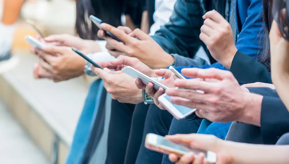 Mehrere Personen sitzen nebeneinander und halten Smartphones in ihren Händen. Einige tragen formelle Kleidung wie blaue Blazer.