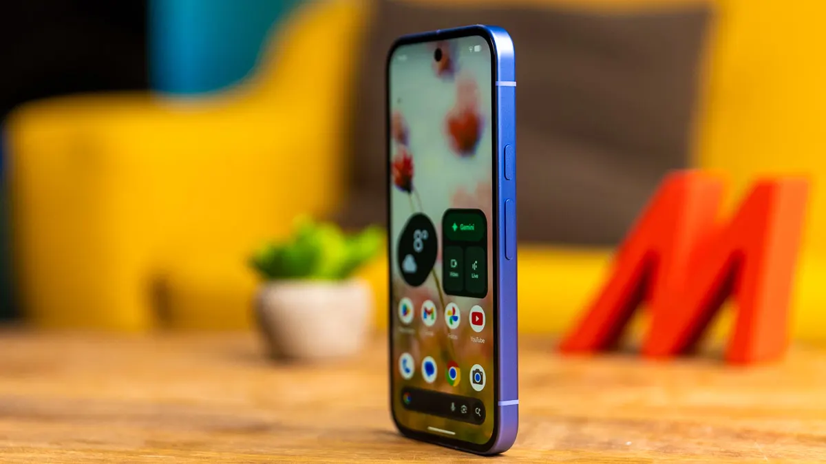 Das Pixel 10a steht mit eingeschaltetem Display auf einem Holztisch, man sieht es leicht seitlich.