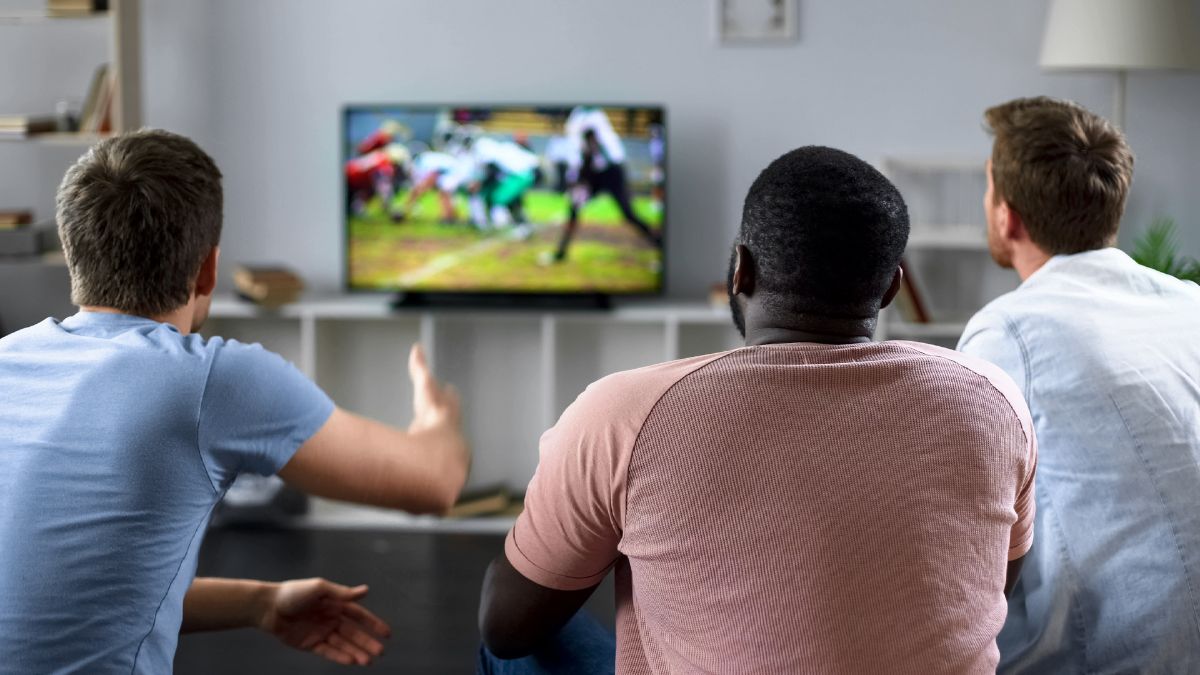 Drei Männer schauen American Football auf einem kleinen Fernseher.
