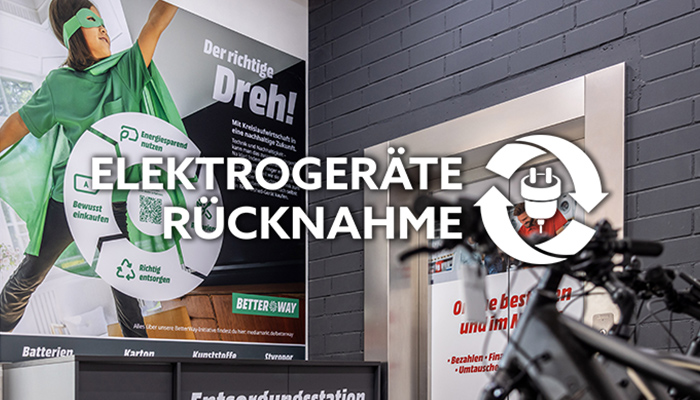 Ein Schild mit der Aufschrift „Elektrogeräte Rücknahme“ neben einem Fahrrad vor einer grauen Ziegelwand. Ein Comic-Superheld ist auch zu sehen.