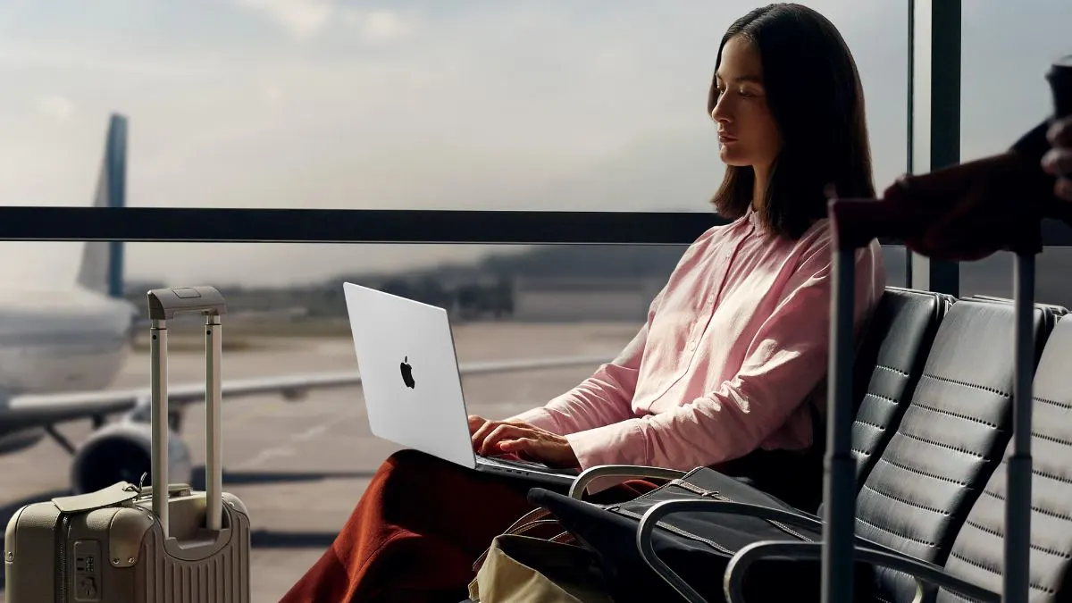 Eine Frau tippt auf dem MacBook Pro 14" M5 im Wartebereich eines Flughafens.