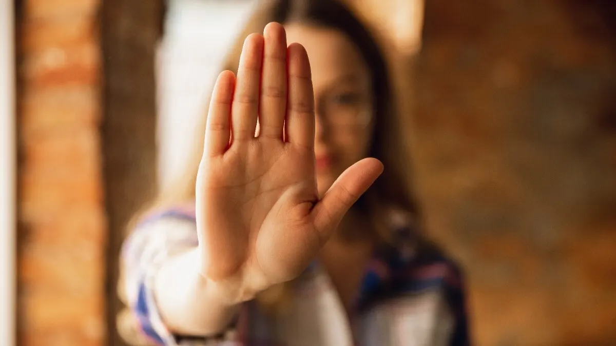 Eine Frau macht eine Stopp-Geste, indem sie die flache Hand in die Kamera hält.