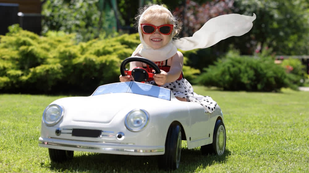 Mädchen mit Sonnenbrille fährt Kinder-Elektroauto und lacht
