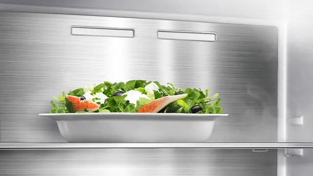 Im Kühlschrank steht eine weiße Schüssel mit grünem Salat, Paprika, schwarzen Oliven und Käse auf einem Regal.