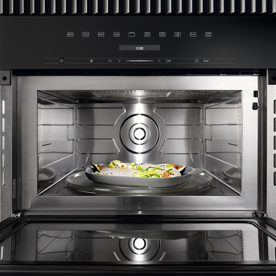 Edelstahl Mikrowelle mit Speisen auf einem Teller innen, gegen einen schwarzen Hintergrund.