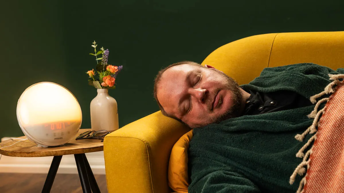 Andreas schläft auf einer Couch, neben ihm steht ein Tageslichtwecker auf einem Beistelltisch.