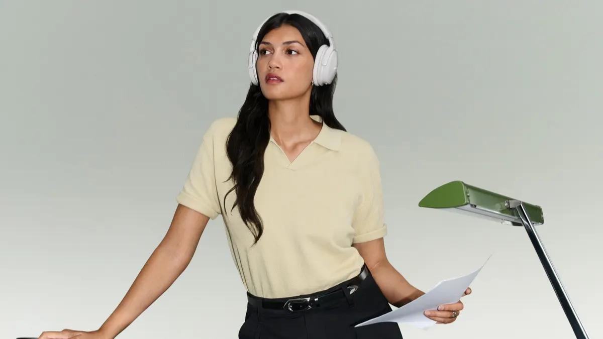 Eine Frau steht an einem Schreibtisch und trägt den Bose QuietComfort Kopfhörer (2. Gen.).