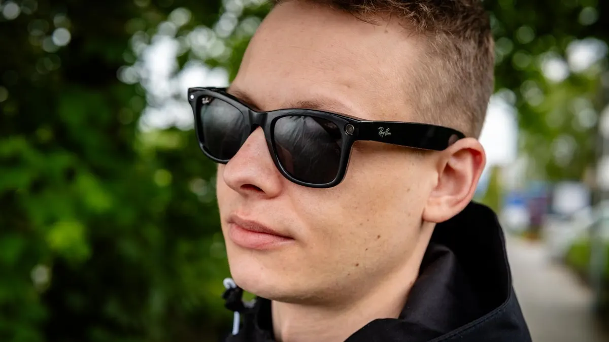 Ein Mann mit dunkler Jacke und schwarzer Sonnenbrille vor grünem Hintergrund.