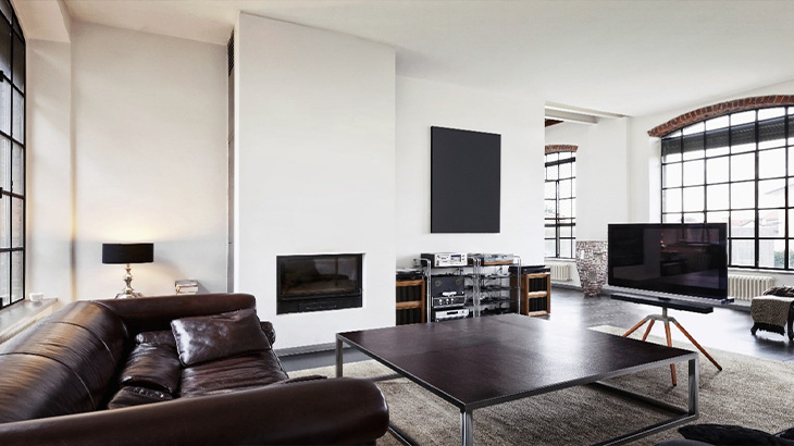 Ein Wohnzimmer mit braunem Ledersofa, schwarzem Couchtisch, Kamin und großem Fenster. Ein Fernseher steht auf einem Stativ.