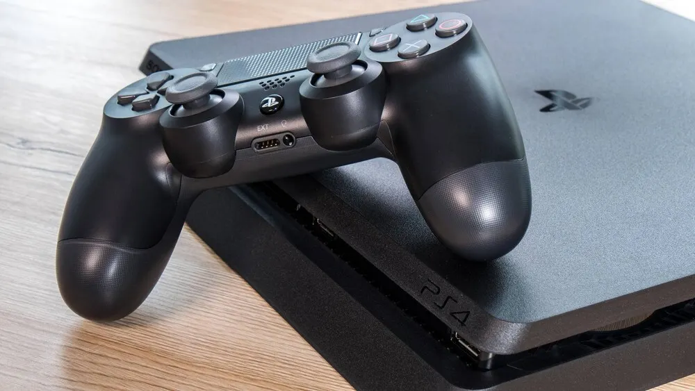 Ein schwarzer PlayStation 4 Controller liegt auf einer schwarzen PlayStation 4 Konsole auf einem Holztisch.