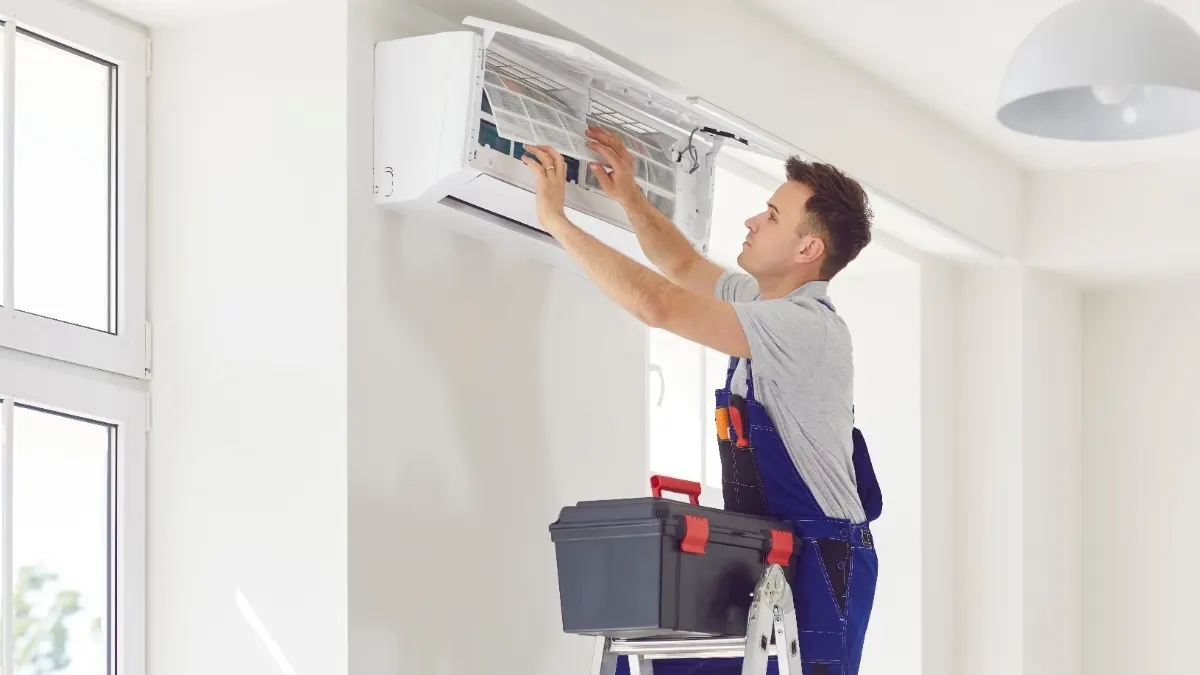 Ein Mann in Handwerkerkleidung installiert eine Split-Klimaanlage.