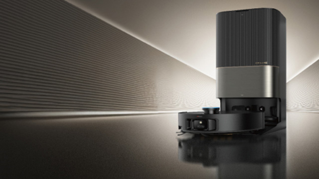 Ein grauer, automatischer Staubsauger mit Ladestation steht vor einem grauen Hintergrund mit dem Markennamen Dreame.