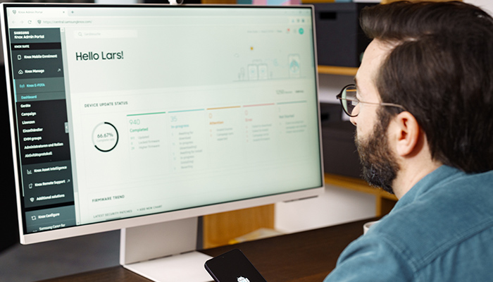 Ein Mann sitzt vor seinem Computer, er hat ein Smartphone in der Hand.