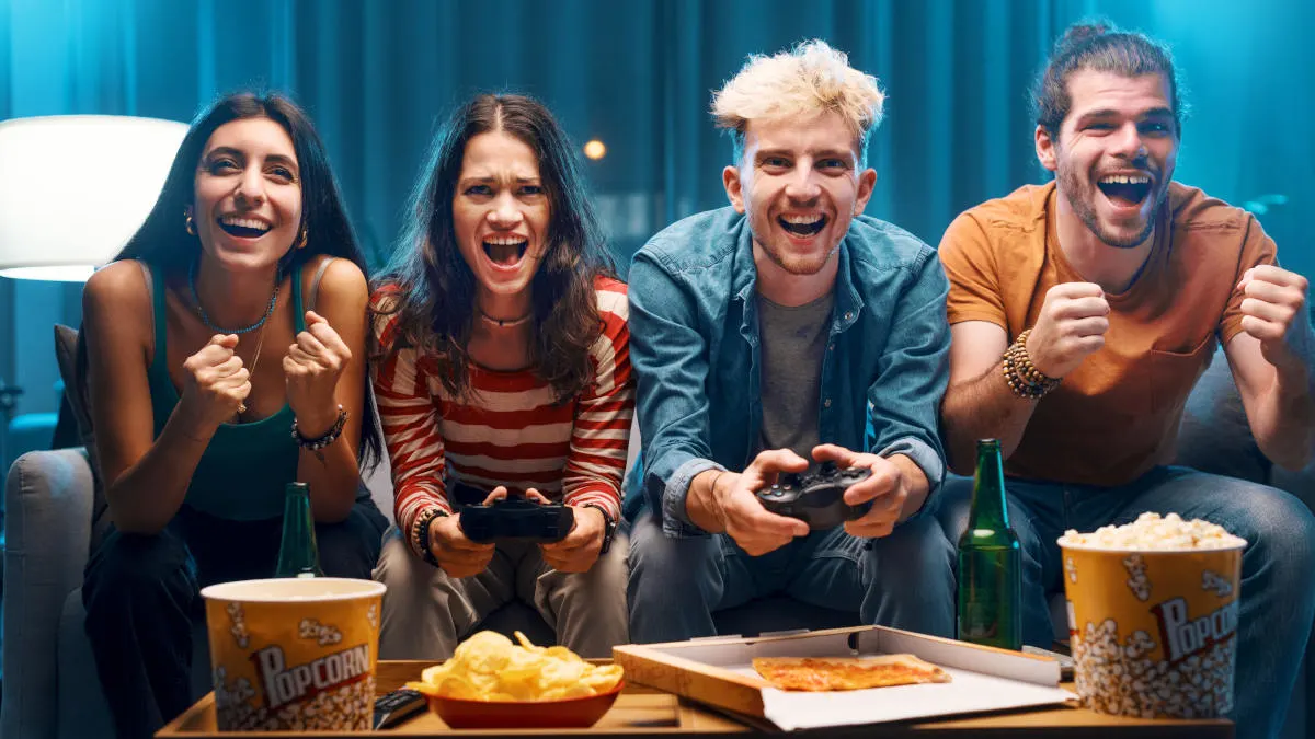 Vier Personen sitzen auf einer Couch und spielen gemeinsam ein Videospiel.