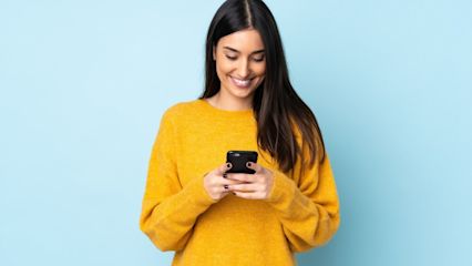 Eine Frau vor einem blauen Hintergrund tippt auf ihr Smartphone