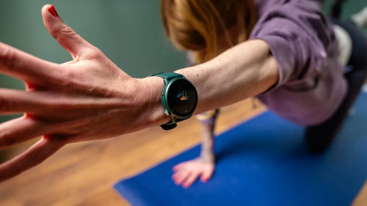 Eine Person auf einer blauen Yogamatte, die eine grüne Smartwatch trägt und eine Dehnübung macht.