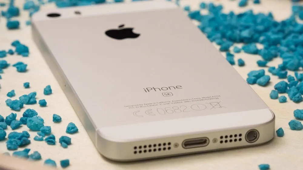 Ein iPhone SE liegt auf einer Fläche mit kleinen, türkisfarbenen Steinen. Das Apple-Logo ist sichtbar.