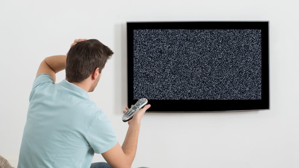 Mann sitzt auf Sofa vor einem Fernseher mit Störbild
