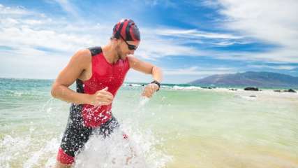 Männlicher Athlet aus dem Meer kommend, schaut auf seine Smartwatch