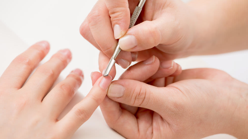 Eine Maniküre schiebt die Nagelhaut bei den Händen einer Kundin zurück.