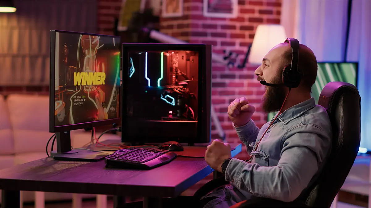 Mann mit Kopfhörern jubelt mit geballten Fäusten vor einem Monitor, auf dem groß Winner steht.