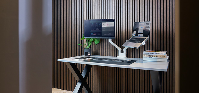 Ein Schreibtisch mit einem Computer, einem Laptop, einer Tastatur, einer Maus, einer Pflanze und Büchern vor einer Wand.