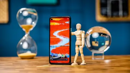Ein Smartphone mit einem roten Bildschirm steht auf einem Tisch, daneben eine Sanduhr, eine Holzpuppe und eine Kristallkugel.