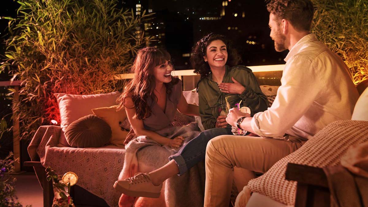 Eine Gruppe von Leuten entspannt sich im Garten auf Gartenmöbeln bei stimmungsvoller Beleuchtung.