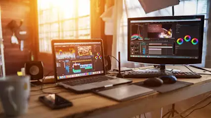 Ein Schreibtisch mit Laptop, Monitor, Maus, Tastatur und Grafiktablett. Bearbeitungssoftware ist auf den Bildschirmen sichtbar.