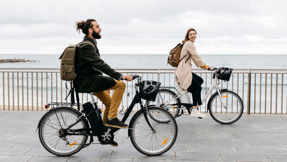 Ein Mann und eine Frau fahren auf Fahrrädern an einem Strand vorbei.