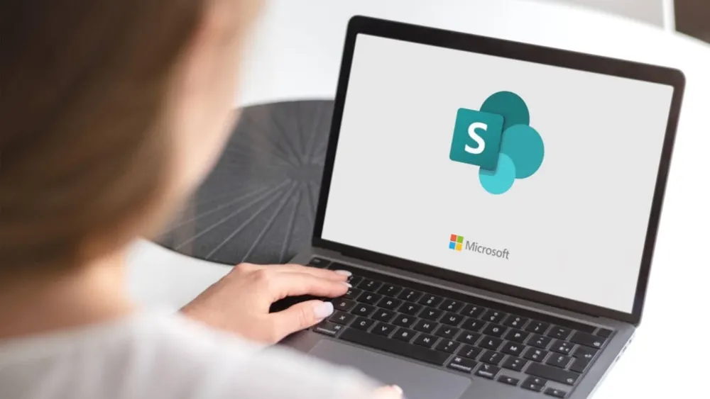 Eine Person tippt auf einem Laptop. Der Bildschirm zeigt das Microsoft SharePoint-Logo.