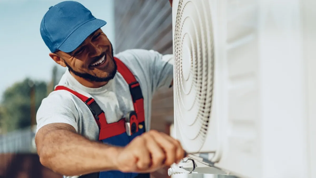 Ein Mann in Arbeitskleidung montiert das Außengerät einer Split-Klimaanlage.