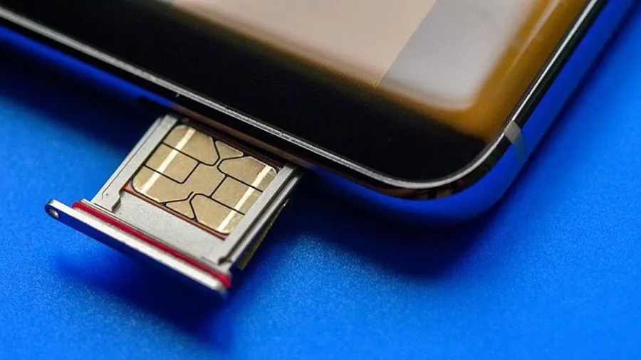Nahaufnahme eines Smartphones mit herausgezogenem SIM-Kartenfach auf blauem Hintergrund. Die SIM-Karte ist goldfarben und rechteckig.
