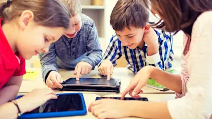 Drei Kinder und eine Lehrerin arbeiten mit Tablets an einem Tisch.