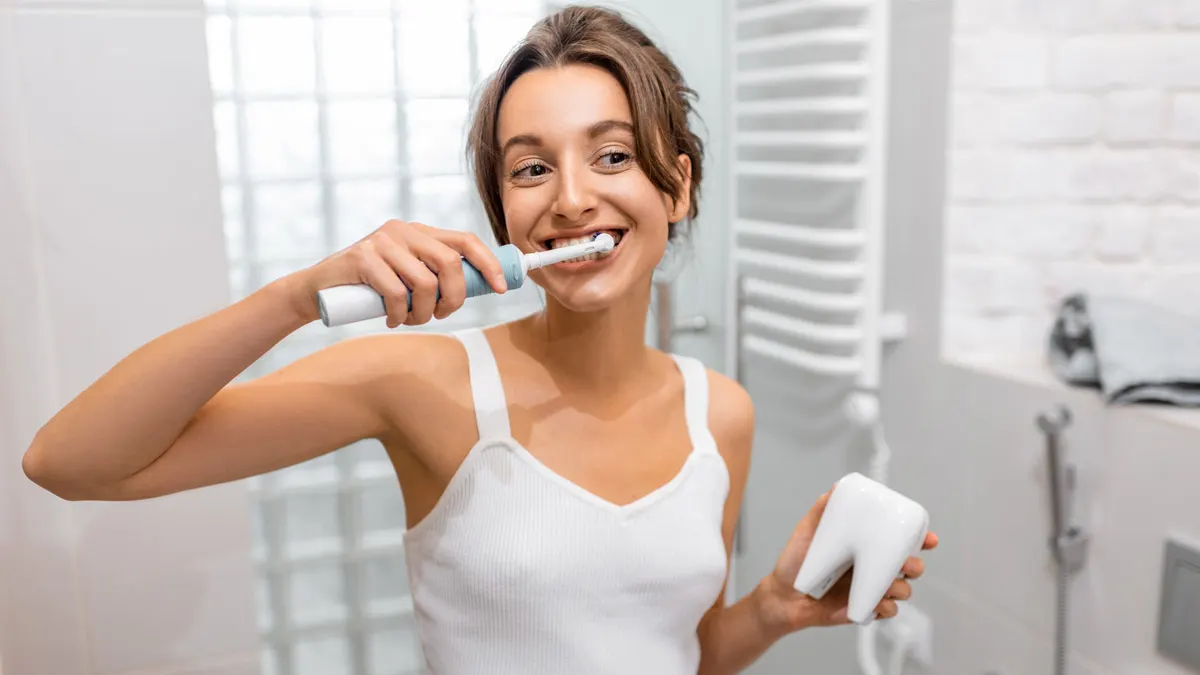 Eine Frau putzt sich mit einer elektrischen Zahnbürste die Zähne. Sie hält die Zahnbürste mit der rechten Hand fest und steht in einem Badezimmer.