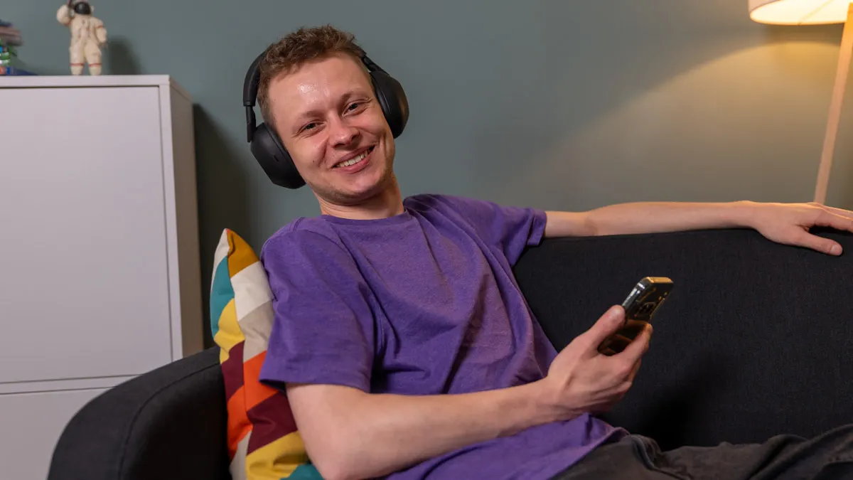 Alex trägt den Kopfhörer Sony WH-1000XM6 und sitzt auf einem Sofa.