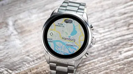 Silberne Smartwatch zeigt eine Karte von Hamburg mit der Uhrzeit 17:17 auf einem hellen Holztisch.