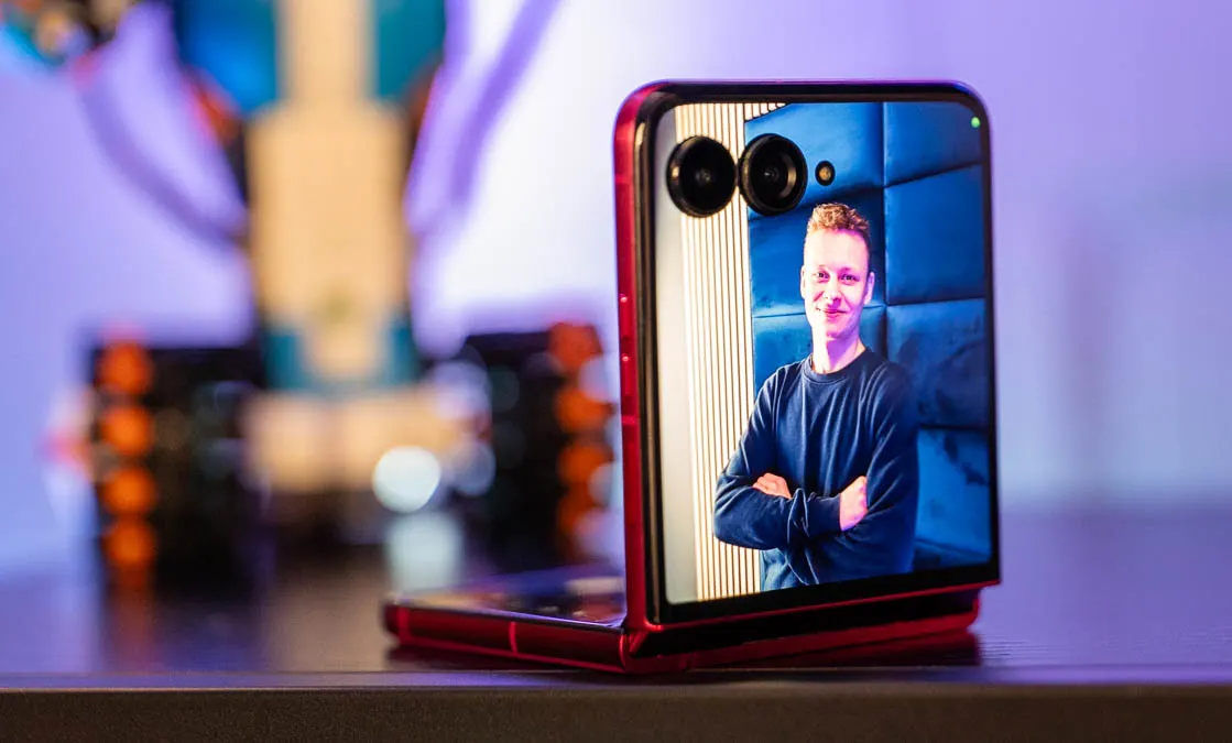 Das Motorola Razr 60 Ultra steht mit im 90-Grad-Winkel aufgeklappten Display auf einem Tisch. In der Kameravorschau auf dem Außendisplay posiert Alex für ein Foto.