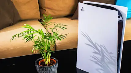 Eine PS5 steht gemeinsam mit einer kleinen Zimmerpflanze auf einem Couchtisch.