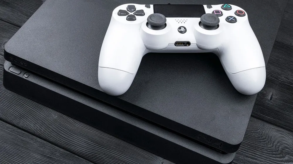 Auf einem dunklen Holzuntergrund liegt eine graue Spielkonsole, auf der ein weißer Controller mit grauen Joysticks platziert ist.