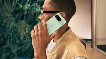 Mann mit Brille telefoniert mit hellgrünem Smartphone vor grünem Hintergrund. Er trägt ein beiges Oberteil.