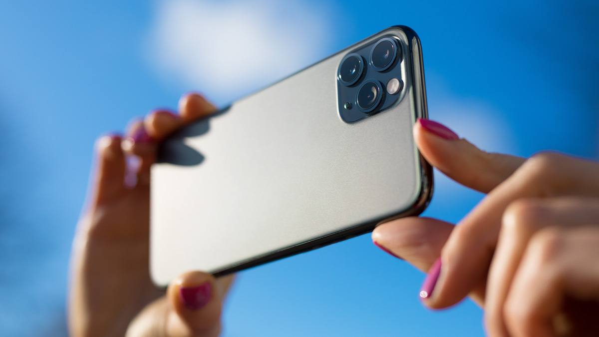 Nahaufnahme eines Smartphones mit drei Kameralinsen und einem Blitzgerät, das von einer Hand gehalten wird.