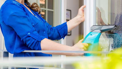 Eine Frau reinigt mit einem Fenstersauger eine Scheibe.