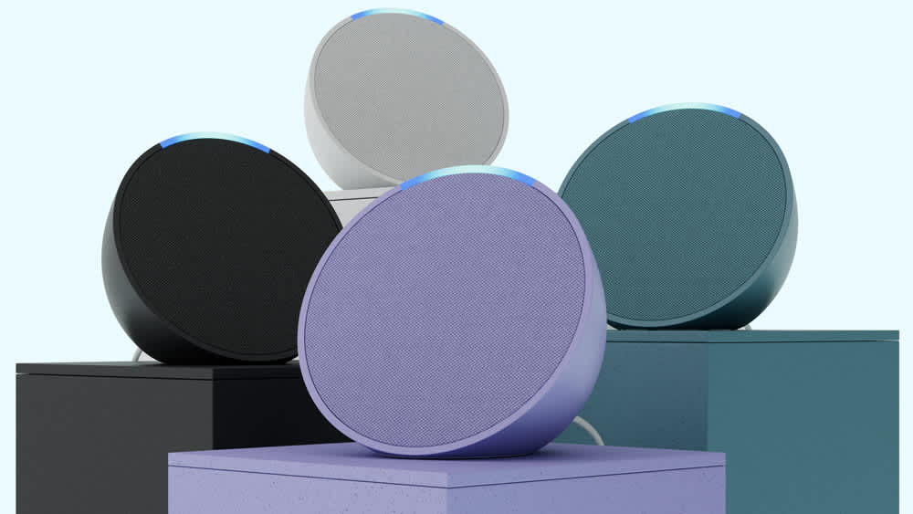 Vier Amazon-Echo-Pop-Geräte in verschiedenen Farben stehen auf unterschiedlich hohen Säulen.