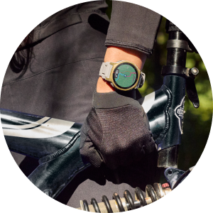 Person mit Smartwatch am Handgelenk und Handschuh, die den Lenker eines Mountainbikes im Gelände festhält.