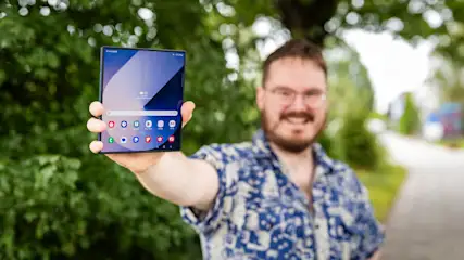 Ein Mann hält ein zusammenklappbares Smartphone mit App-Symbolen vor einem grünen Hintergrund.