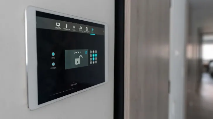 Ein Tablet an der Wand zeigt ein Entsperrsymbol und ein Tastenfeld. Symbole für TV, Licht und Temperatur sind oben sichtbar.
