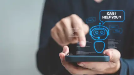 Eine Person interagiert mit einem Smartphone, das eine blaue Chatbot-Schnittstelle mit der Frage "CAN I HELP YOU?" anzeigt.